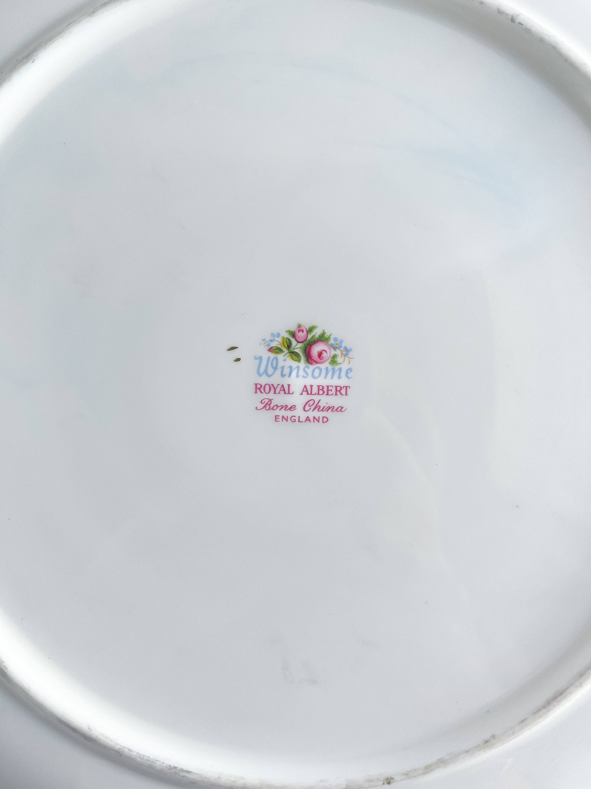 A close-up view of the underside of the Royal Albert Winsome handled cake plate, featuring the authentic backstamp with the pattern name 'Winsome' in blue script, 'ROYAL ALBERT Bone China ENGLAND', and the crown logo.