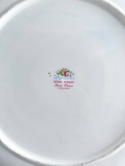 A close-up view of the underside of the Royal Albert Winsome handled cake plate, featuring the authentic backstamp with the pattern name 'Winsome' in blue script, 'ROYAL ALBERT Bone China ENGLAND', and the crown logo.