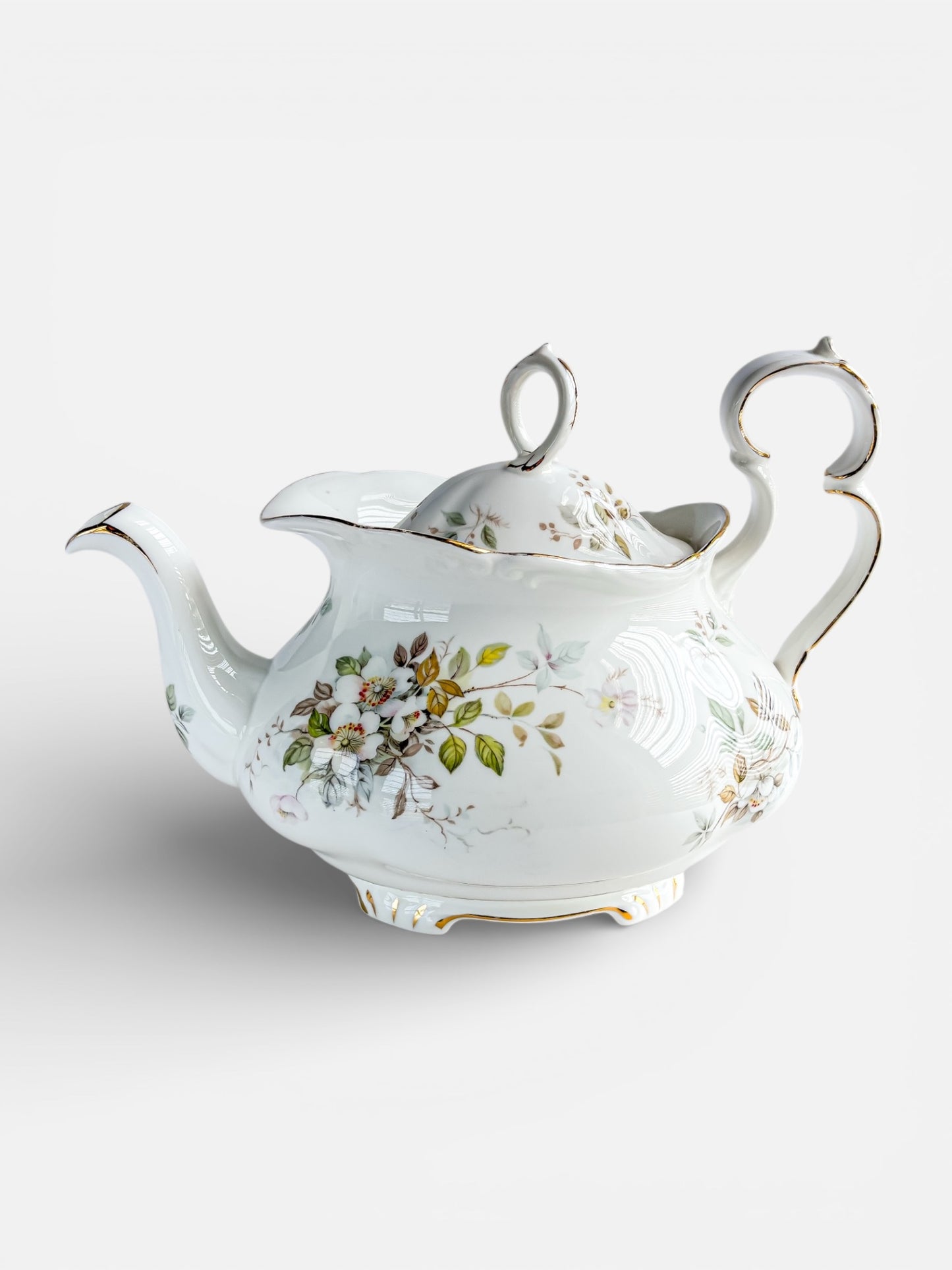 Decorative vintage porcelain teapot with floral design and gold accents on white background