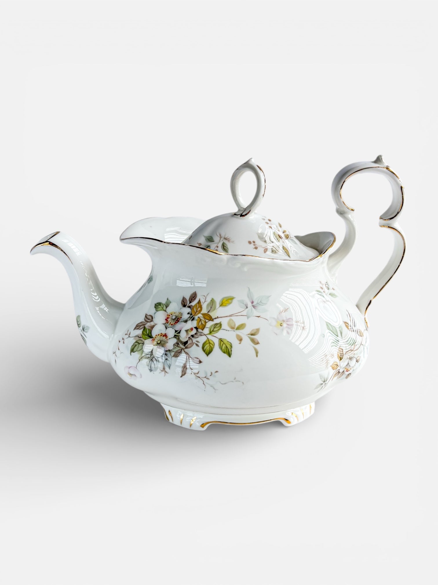 Decorative vintage porcelain teapot with floral design and gold accents on white background