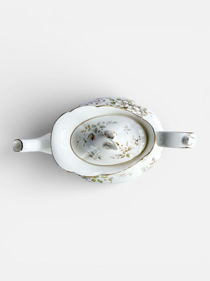 White porcelain teapot with floral and gold trim detail on white background