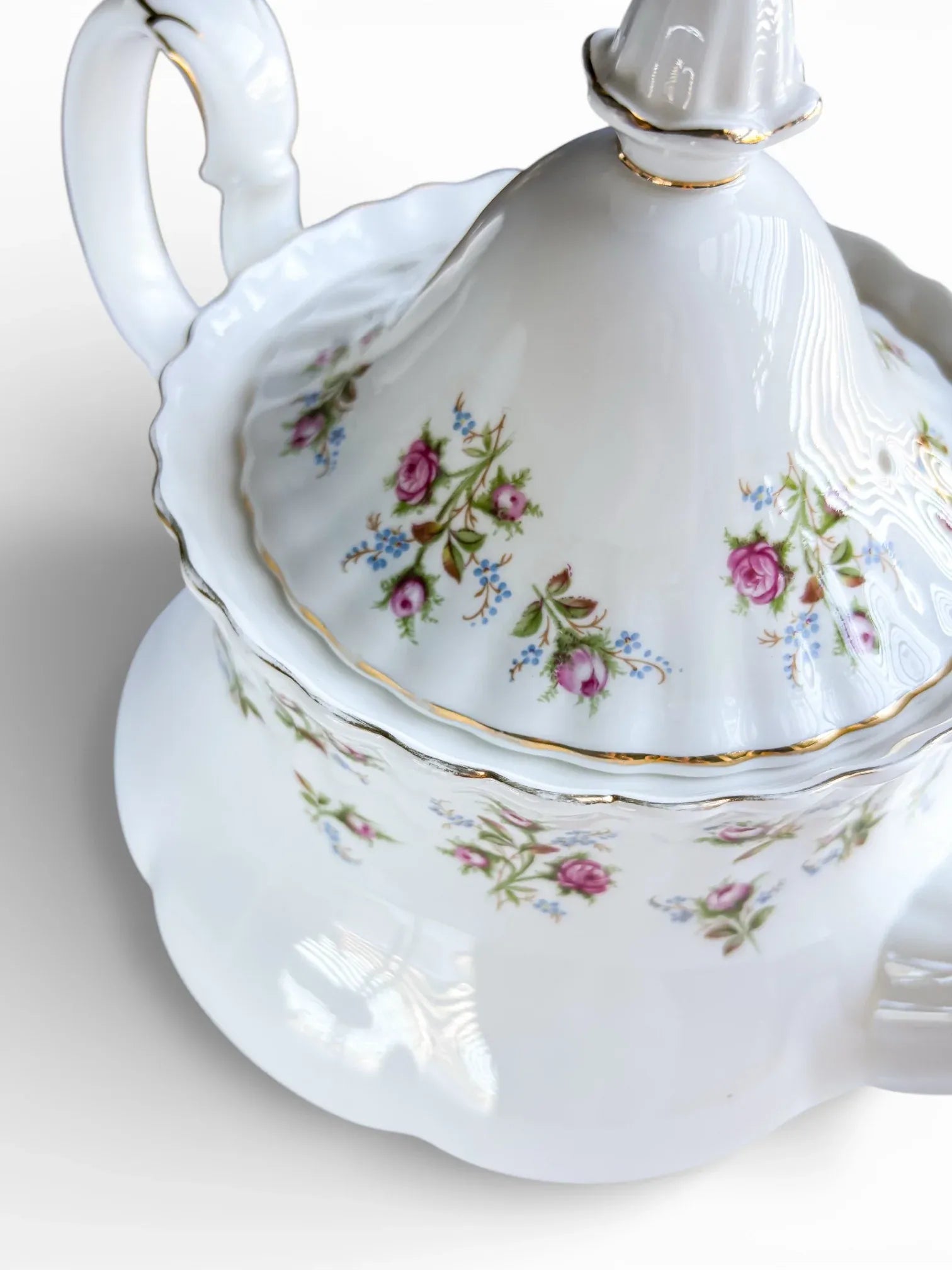 Close-up of the teapot's side showing the floral decoration, steam vent, and gold-trimmed finial.