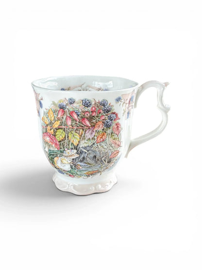 Fine bone china Royal Doulton Brambly Hedge Autumn beaker against a white background, featuring a scalloped foot, scrolled handle, and detailed illustration of Primrose Woodmouse among wild blackberries and rosehips.