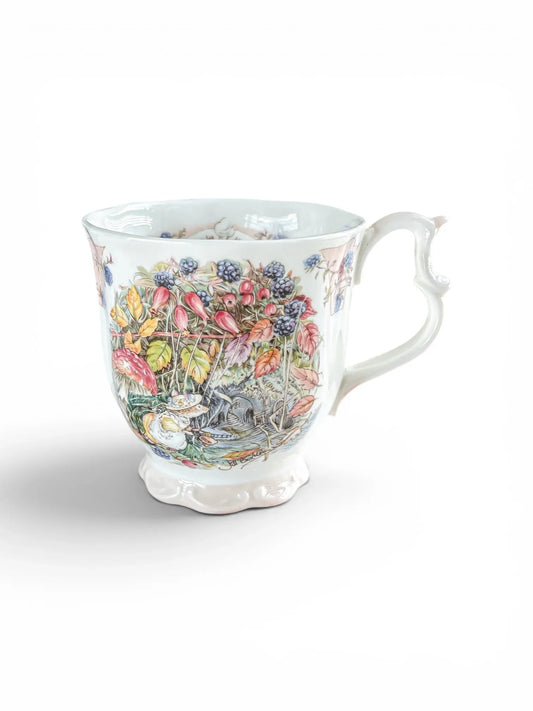 Fine bone china Royal Doulton Brambly Hedge Autumn beaker against a white background, featuring a scalloped foot, scrolled handle, and detailed illustration of Primrose Woodmouse among wild blackberries and rosehips.