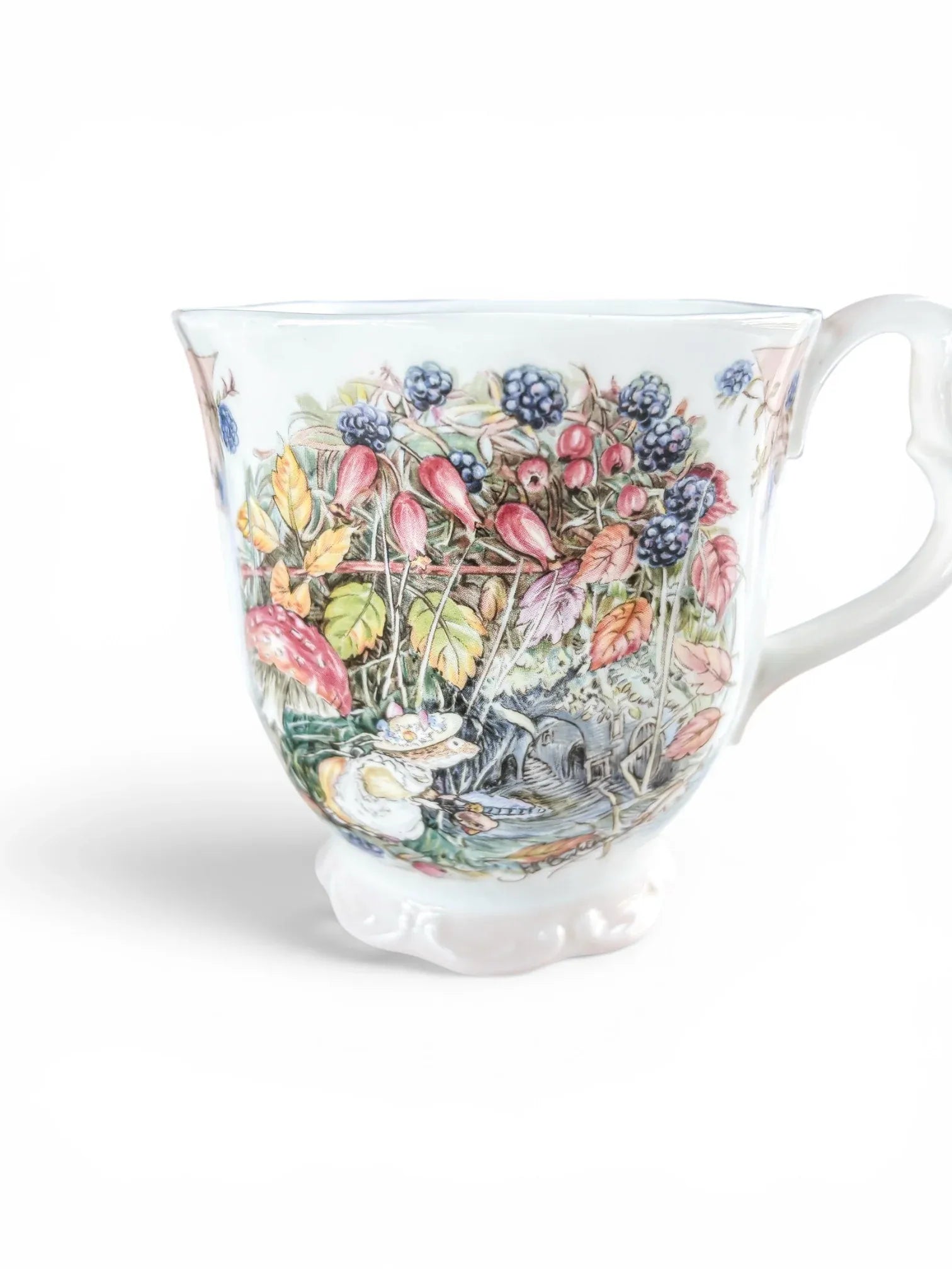 Close-up of the harvest illustration on a Royal Doulton Brambly Hedge Autumn beaker, highlighting the vibrant blackberries, autumn leaves, and the signature baby pink decorative ribbon along the rim.