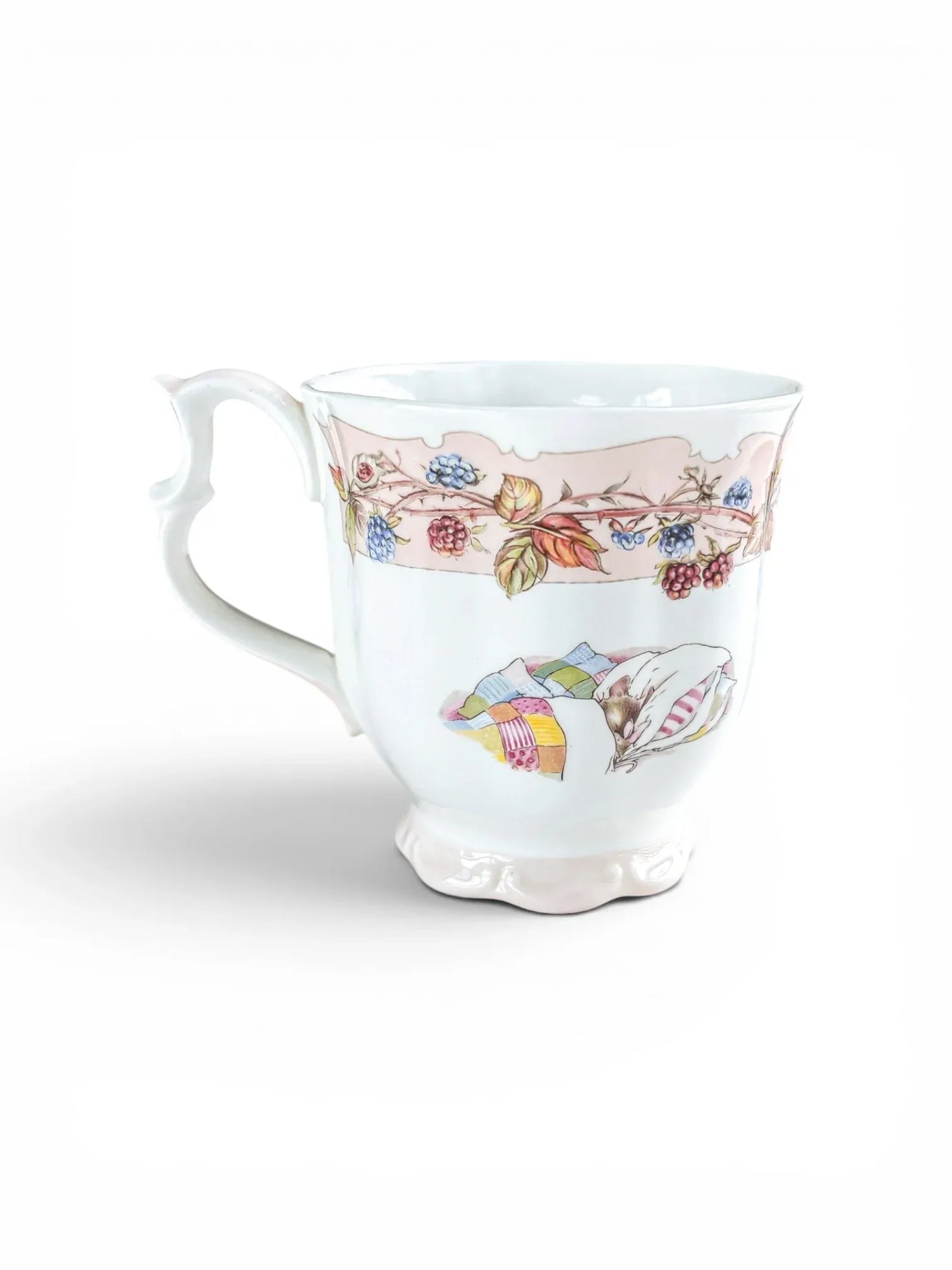 Reverse view of the Royal Doulton Autumn beaker against a white background, featuring a charming illustration of a field mouse resting under a colourful patchwork quilt, set below the signature baby pink decorative ribbon.