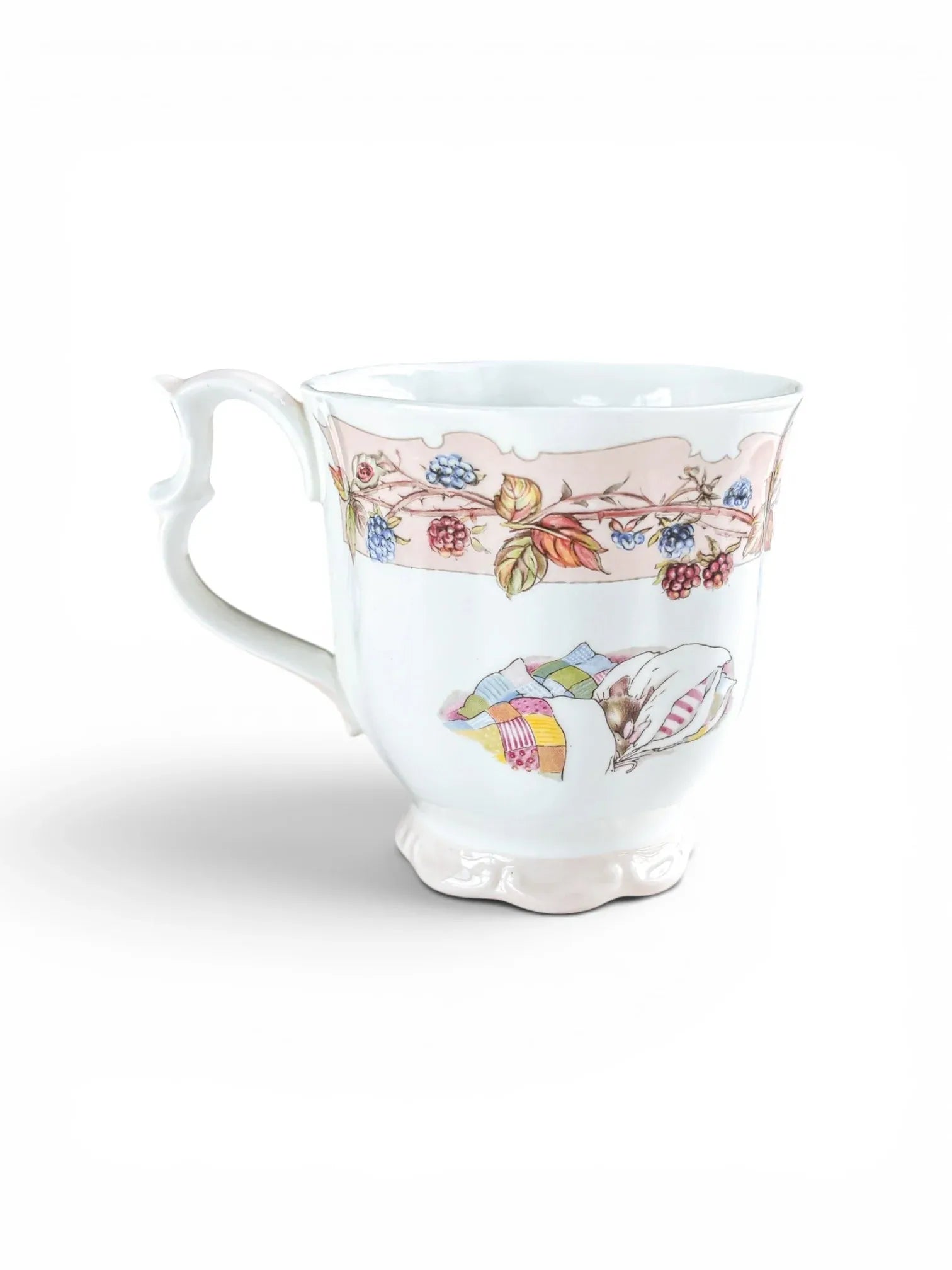 Reverse view of the Royal Doulton Autumn beaker against a white background, featuring a charming illustration of a field mouse resting under a colourful patchwork quilt, set below the signature baby pink decorative ribbon.