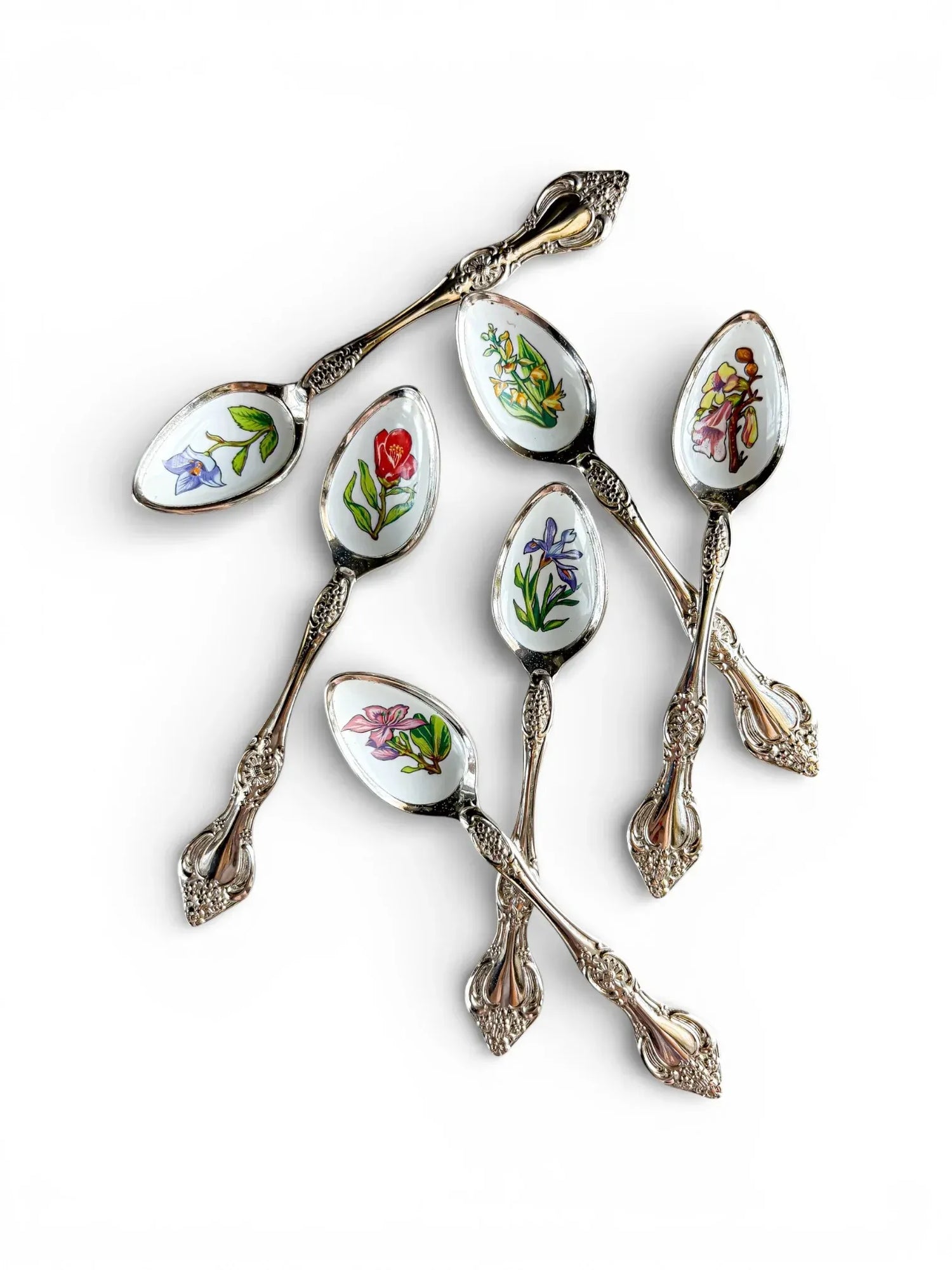 A set of six vintage silver-plated teaspoons from the High Tea & Heritage collection, featuring colourful enamel botanical illustrations of Hong Kong flowers on a white background.