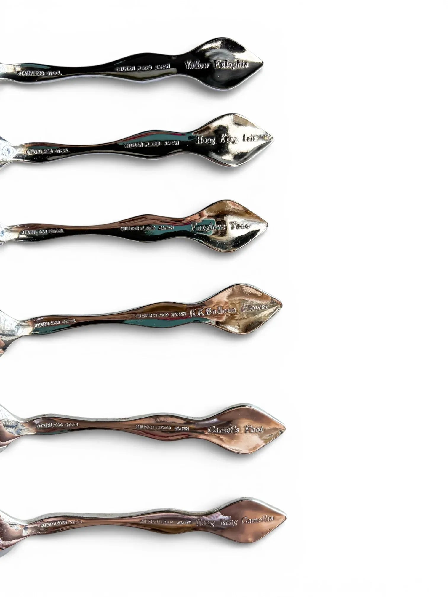 The reverse side of vintage Japanese teaspoons showing engraved botanical names and 'Silver Plated Japan' and 'Stainless Steel' hallmarks.