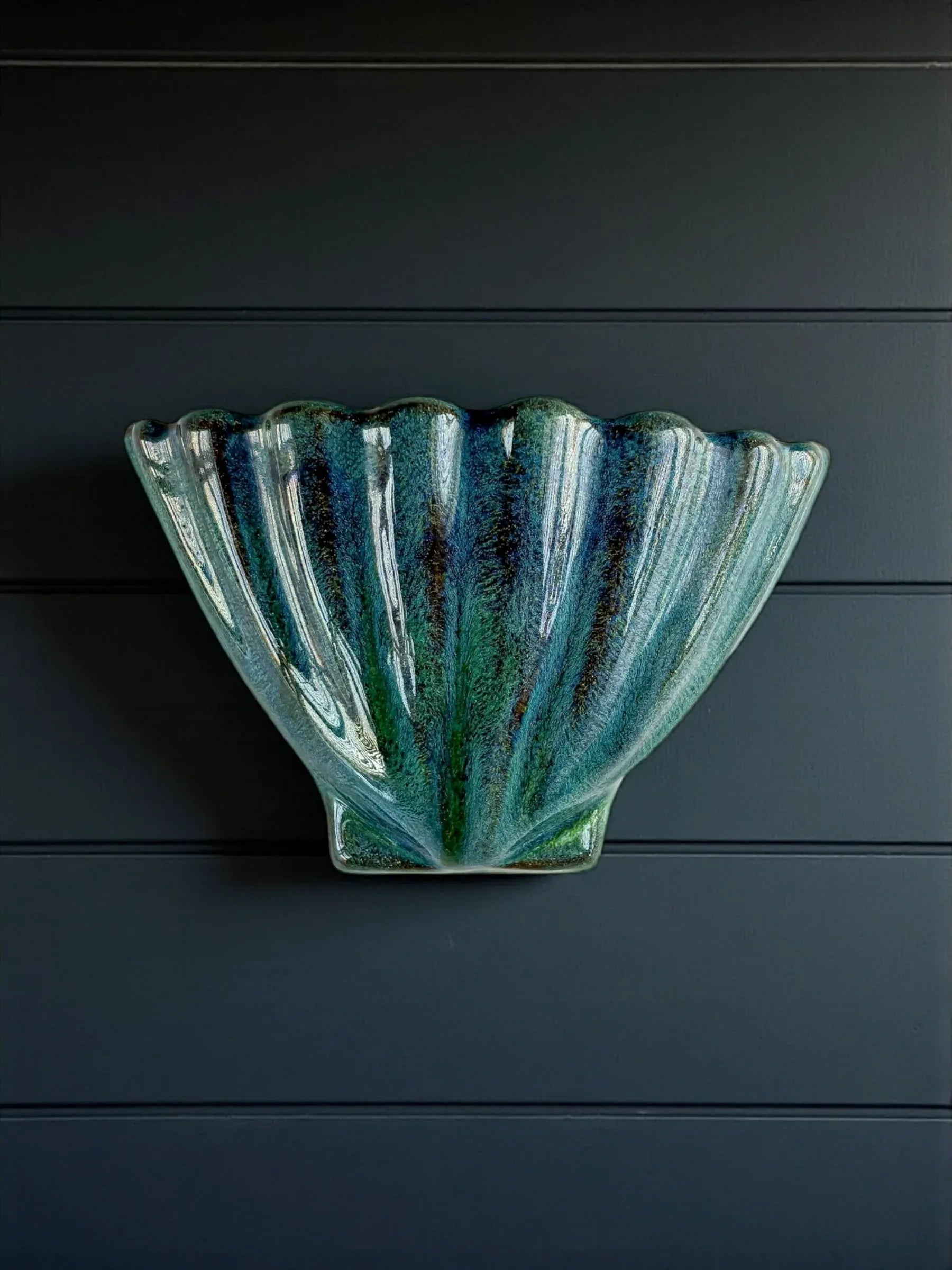 Decorative green and blue ceramic wall vase shaped like a scallop shell on dark paneled wall
