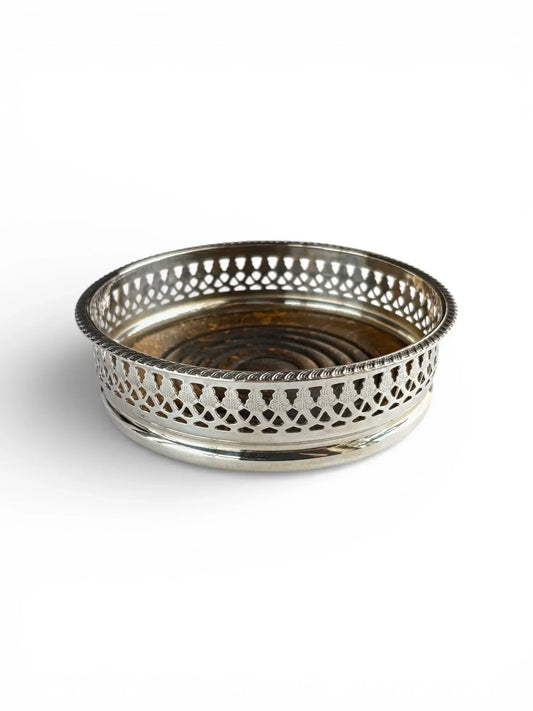 Angled view of a silver-plated vintage wine coaster displaying both the reticulated metal rim and the rich wooden interior.
