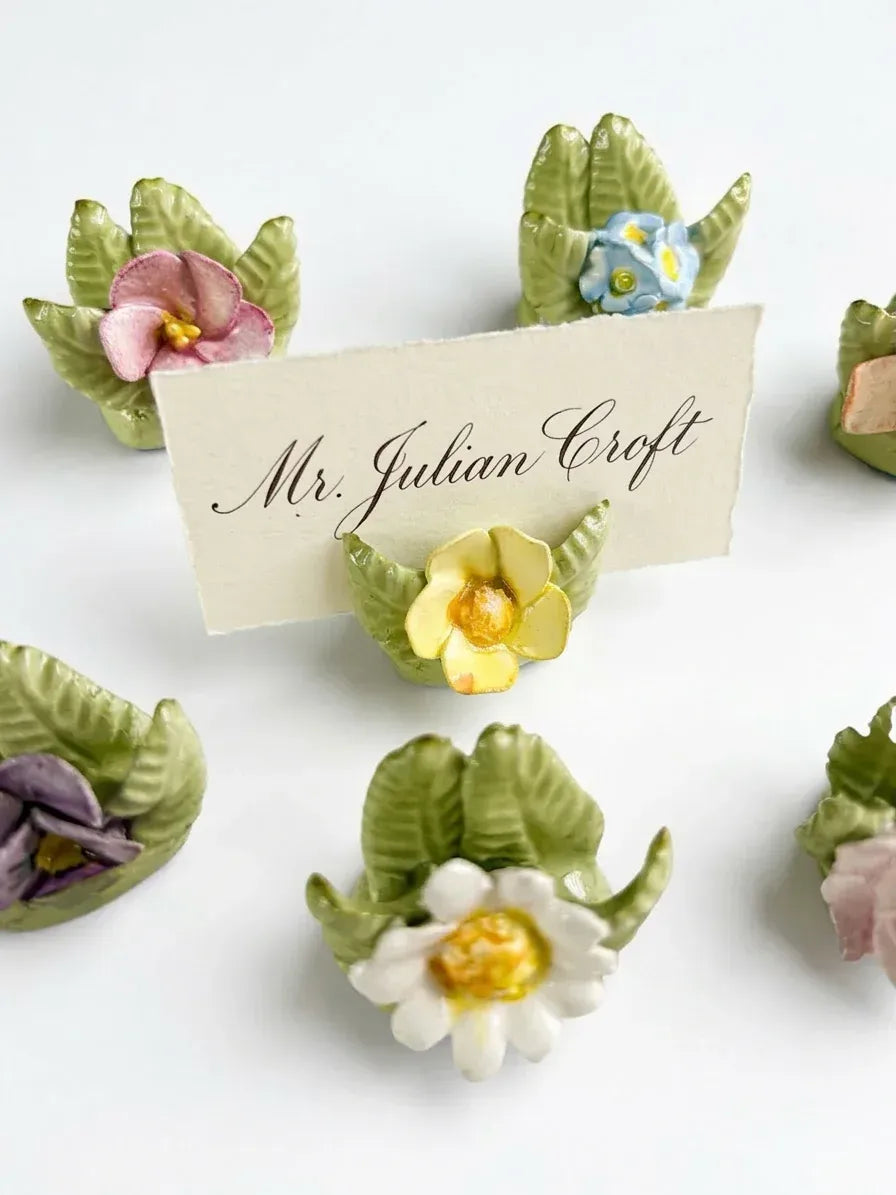 Close-up of a hand-painted porcelain flower holder with a handwritten calligraphy place card for an afternoon tea table setting.