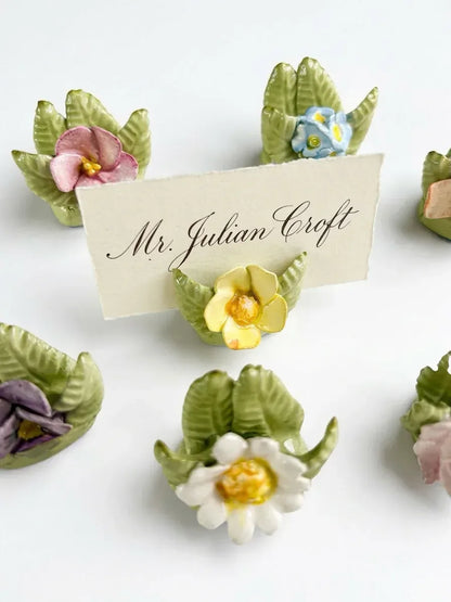 Close-up of a hand-painted porcelain flower holder with a handwritten calligraphy place card for an afternoon tea table setting.