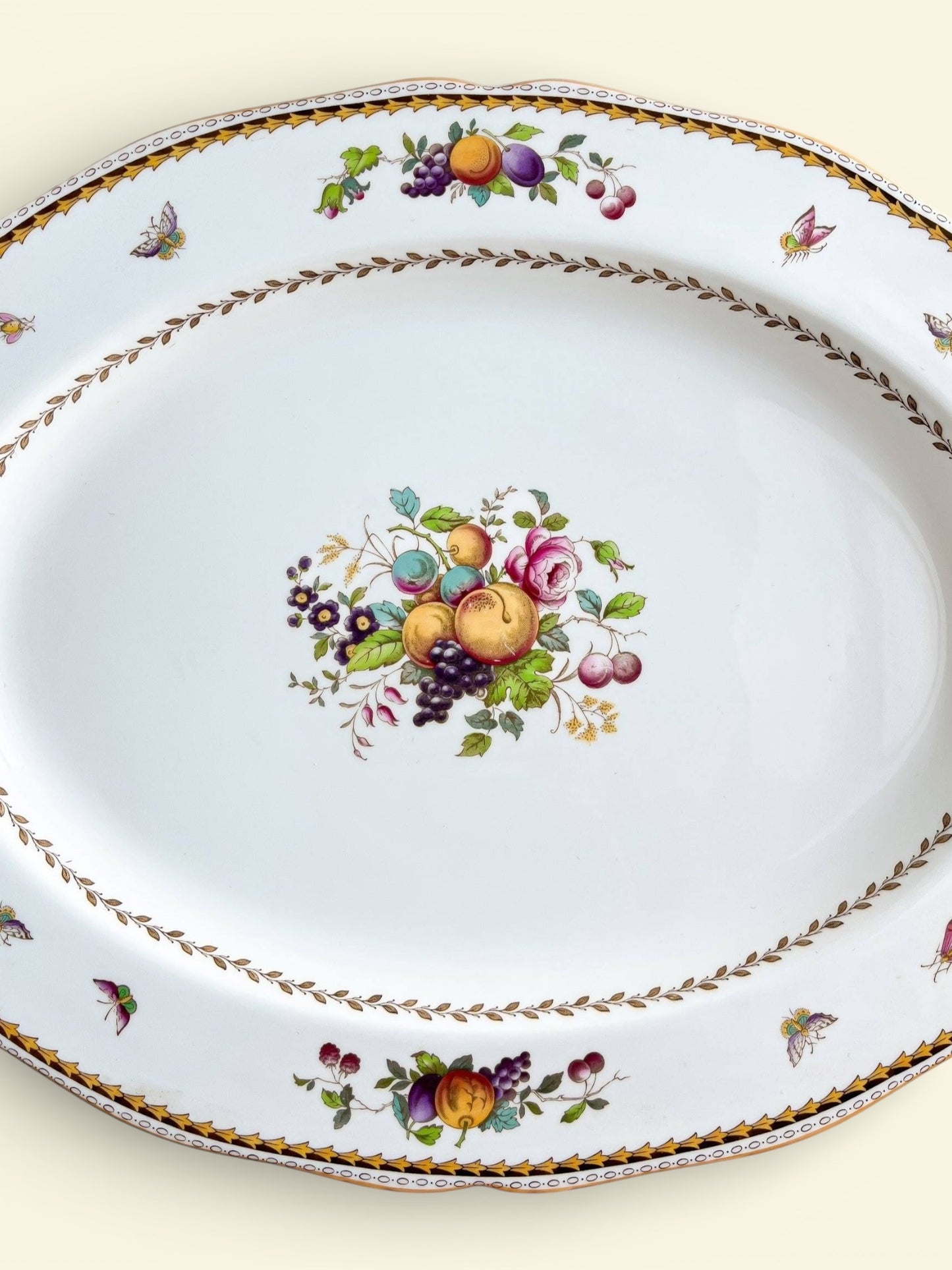 Vintage porcelain serving platter with colorful fruit and floral patterns, decorative butterflies, and gold trim