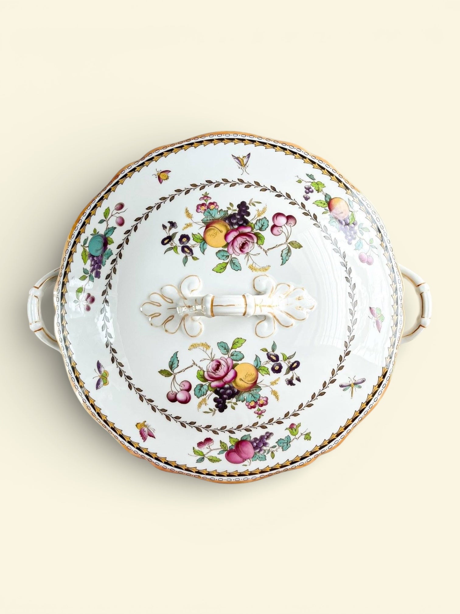 Vintage porcelain covered serving dish with floral and fruit pattern and gold accents on a light background