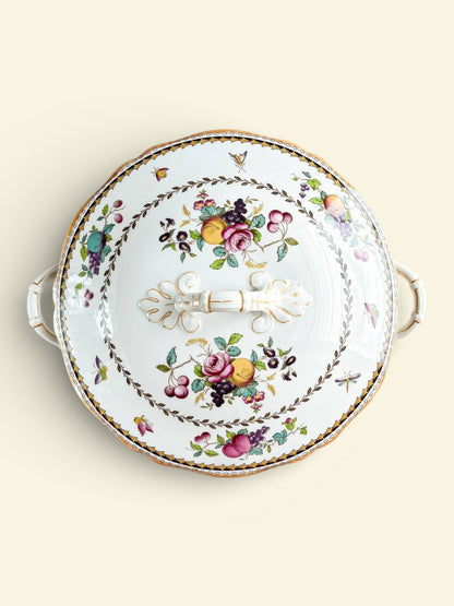 Vintage porcelain covered serving dish with floral and fruit pattern and gold accents on a light background