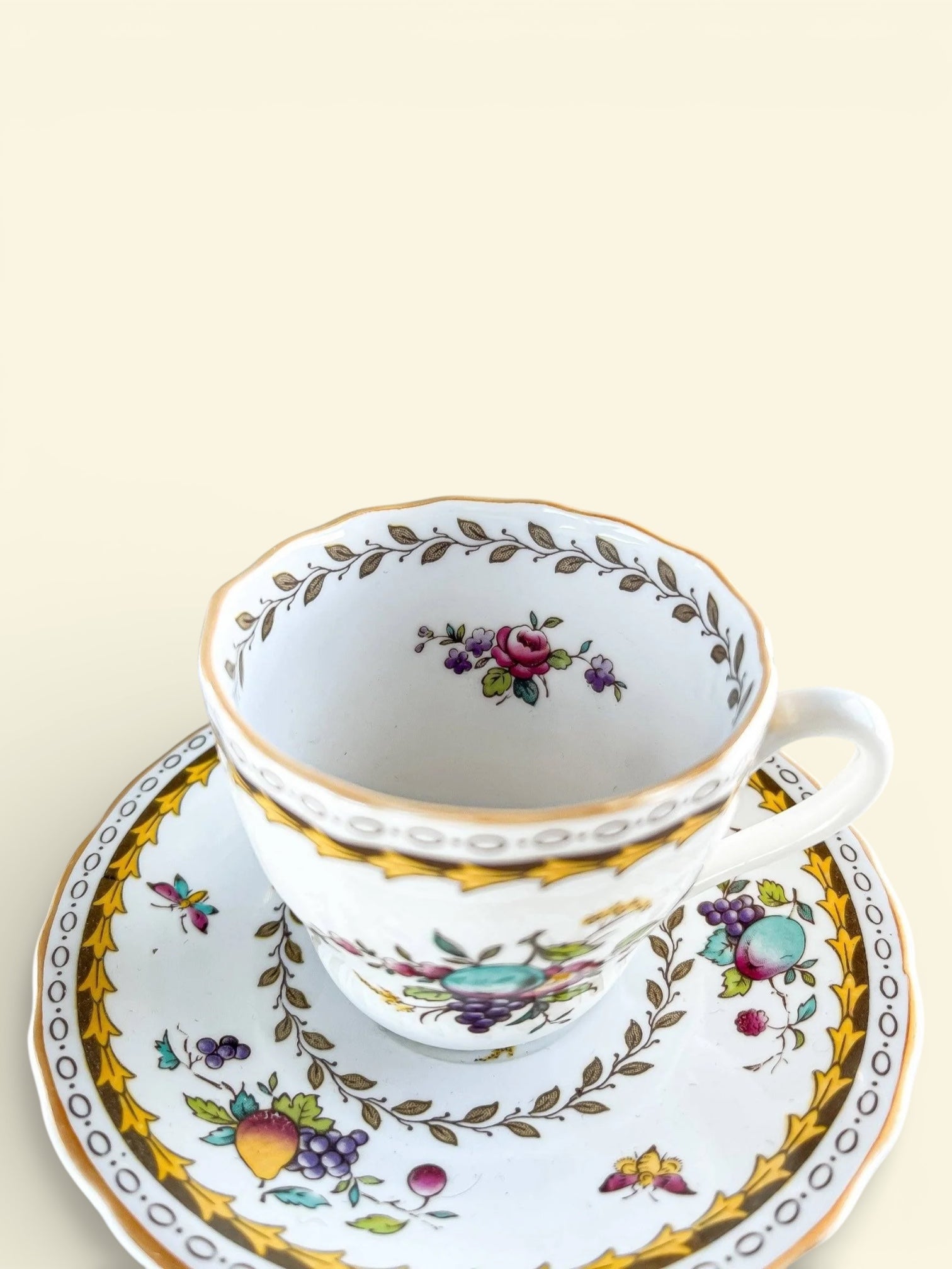 Vintage porcelain teacup and saucer with floral and fruit patterns and gold accents