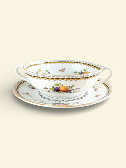 Vintage porcelain double-handled cup and saucer with gold trim and fruit floral pattern on soft beige background