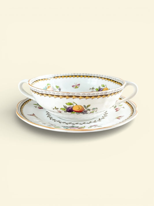 Vintage porcelain double-handled cup and saucer with gold trim and fruit floral pattern on soft beige background