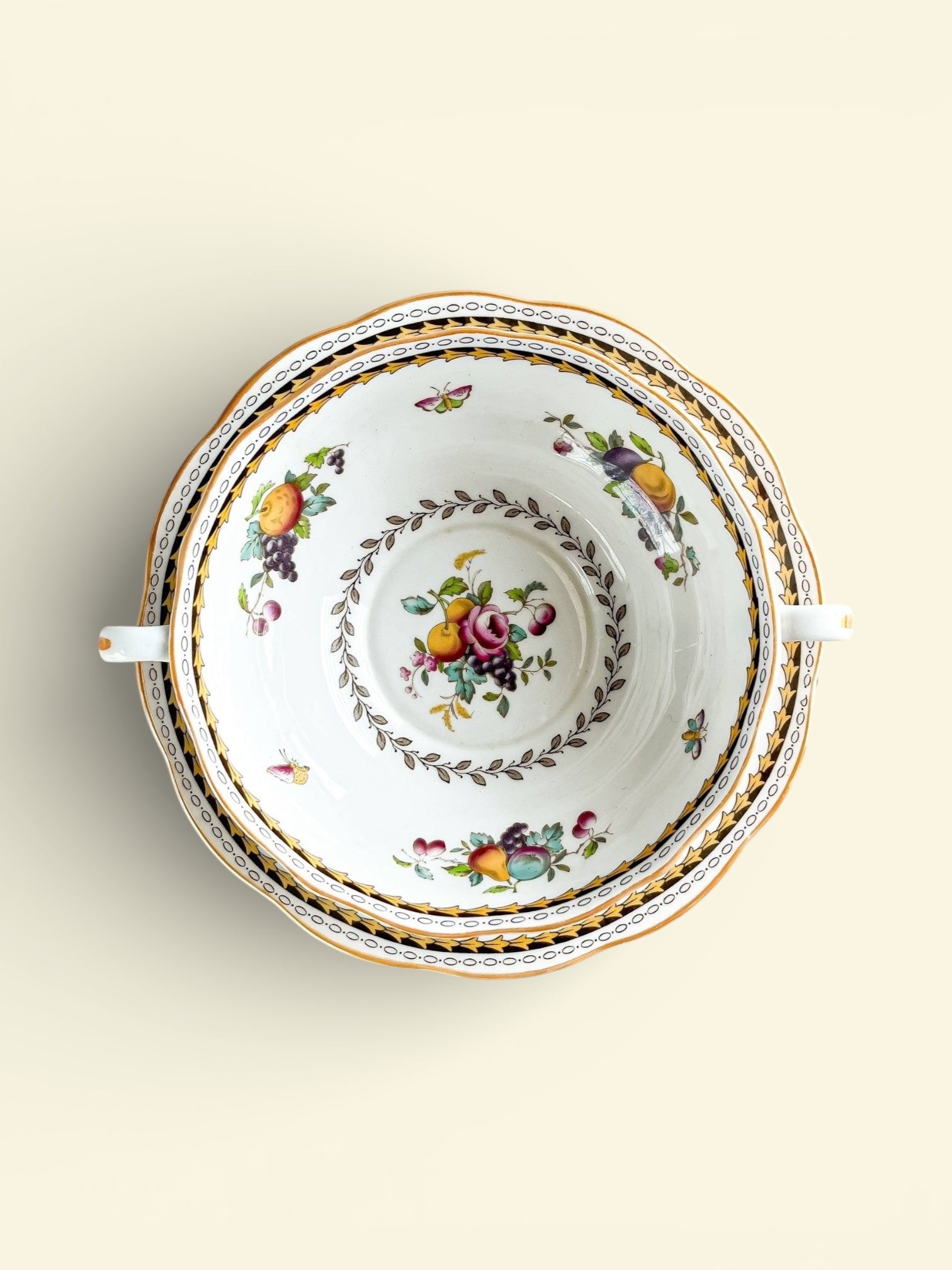 Top view of vintage porcelain bowl with ornate fruit and butterfly floral design and gold trim handles
