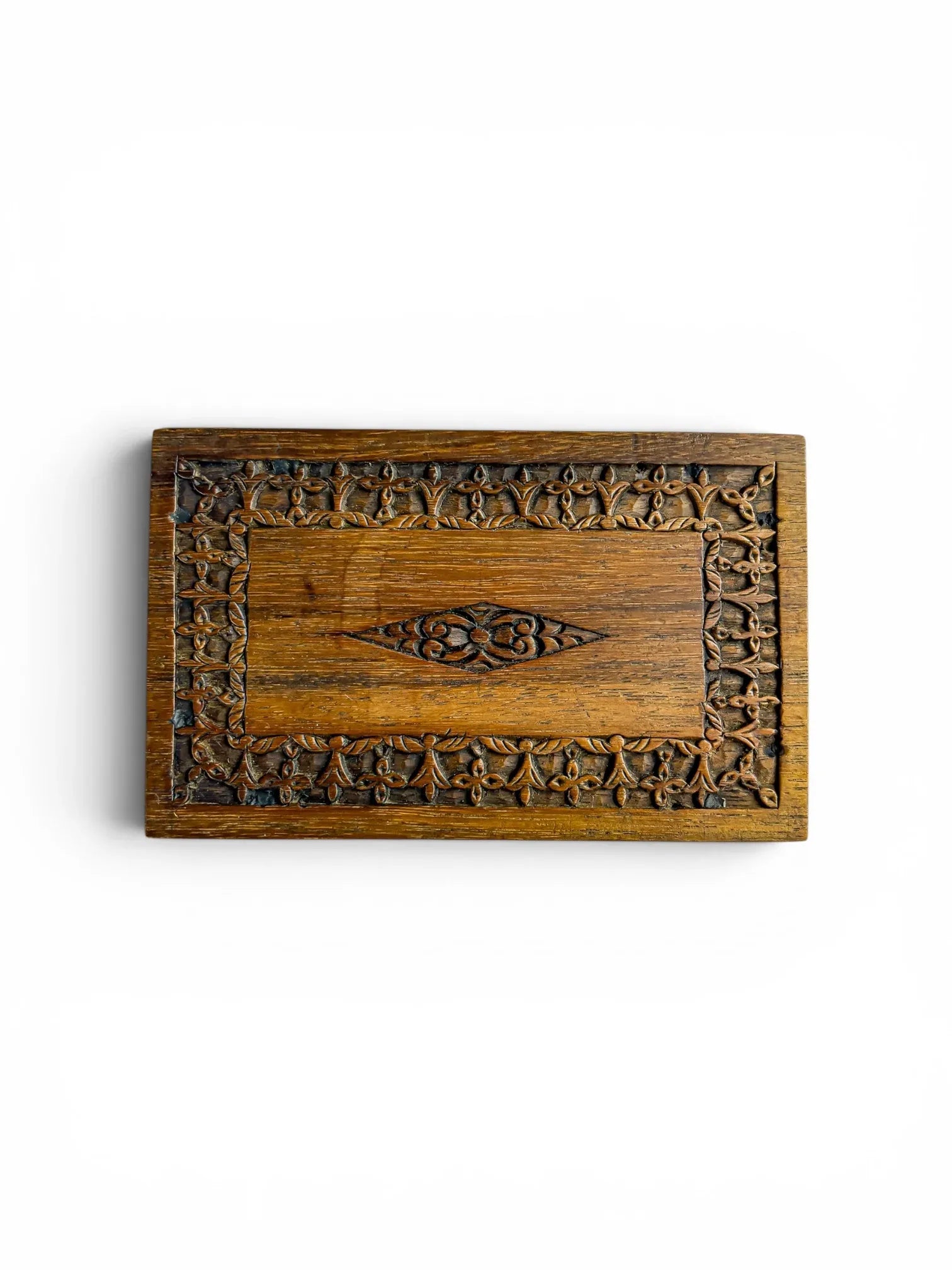 High-angle overhead view of a vintage carved wooden box on a plain white background, highlighting a flat top panel with an intricate repeating foliate border and a central diamond-shaped floral motif.