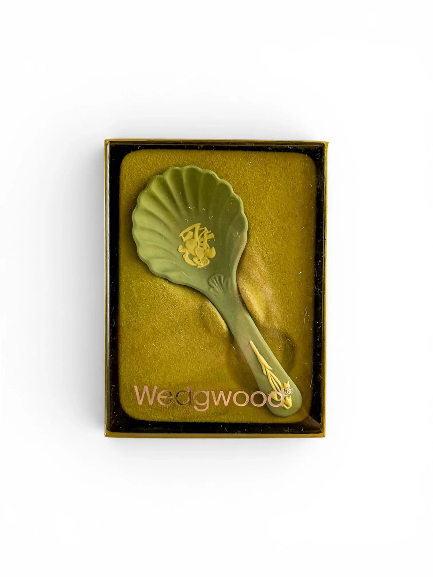 A pale blue Wedgwood Jasperware shell caddy spoon presented in its original box with a clear lid. The "Wedgwood" brand name is printed in silver  across the bottom of the packaging, showcasing the heritage "Cupid Sharpening his Arrow" design in a different colourway.