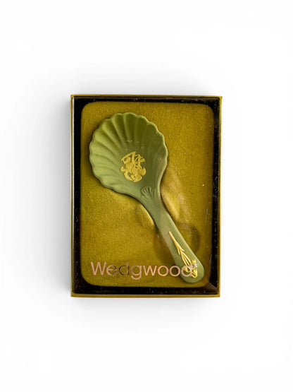 A pale blue Wedgwood Jasperware shell caddy spoon presented in its original box with a clear lid. The "Wedgwood" brand name is printed in silver  across the bottom of the packaging, showcasing the heritage "Cupid Sharpening his Arrow" design in a different colourway.
