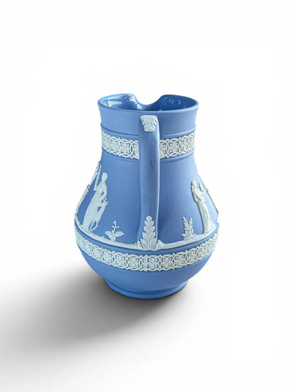 Rear view of a mid-century blue Wedgwood Jasperware Etruscan pitcher, highlighting the handle design. The matte light blue stoneware handle is adorned at the top and base with elegant, hand-applied white acanthus leaf relief work, centred between classical sprigged figures on either side.
