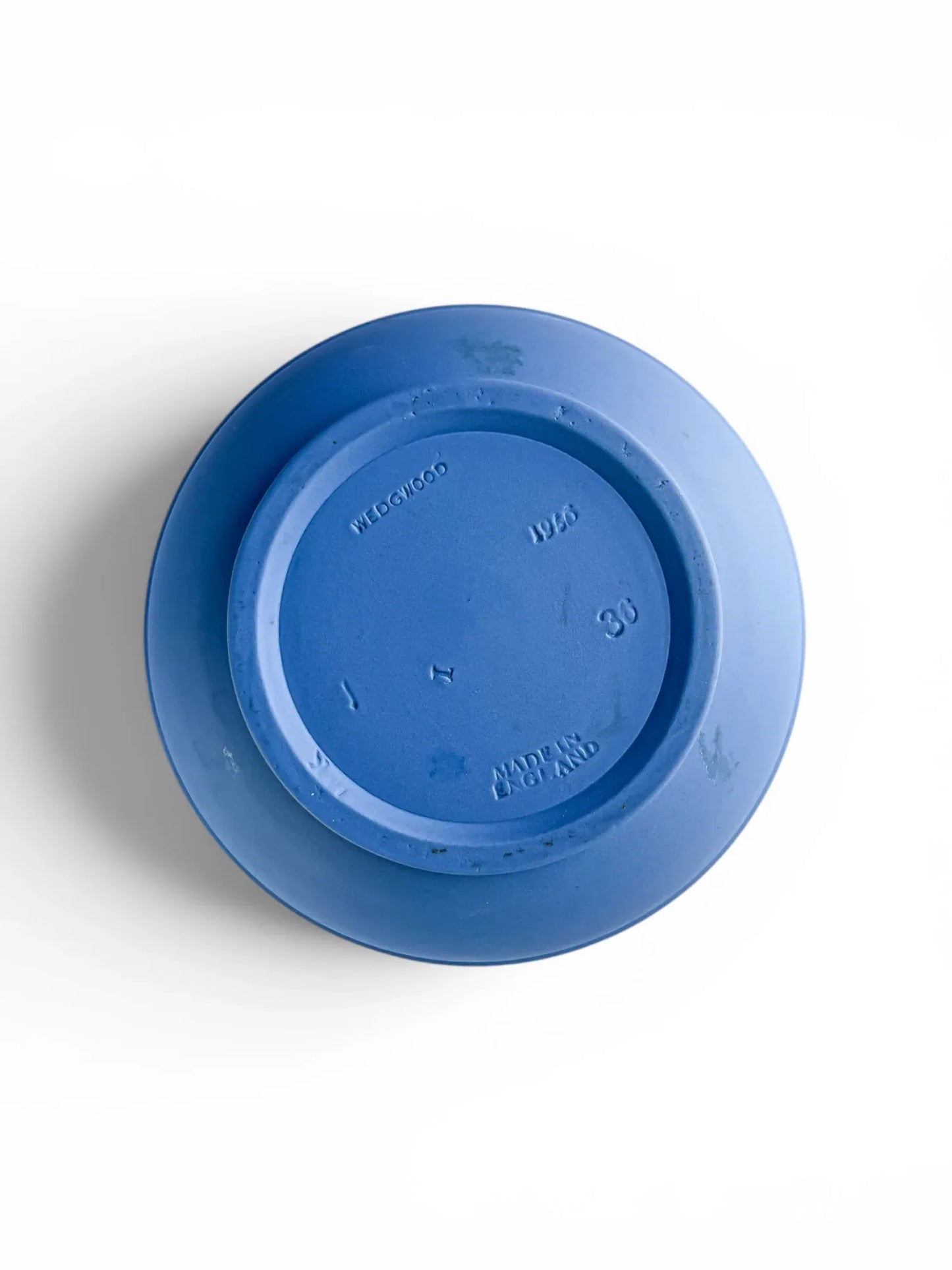 The unglazed exterior base of a vintage blue Wedgwood Jasperware jug, showing authentic impressed maker's marks. The clear stamps include "WEDGWOOD", "MADE IN ENGLAND", the production year "1956", the size number "30", and smaller individual artisan potter marks.