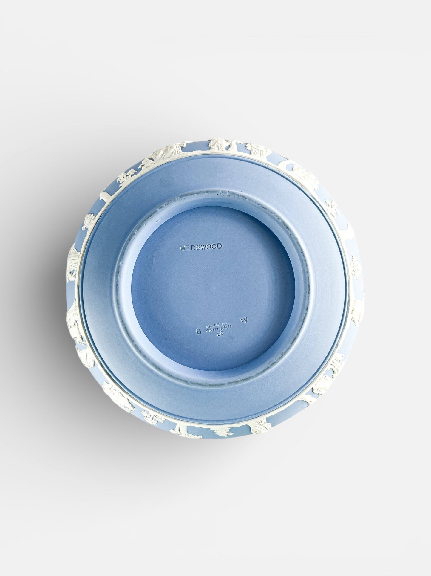 Top view of a blue Wedgwood porcelain plate with white relief decorations around the edge, marked Made in England