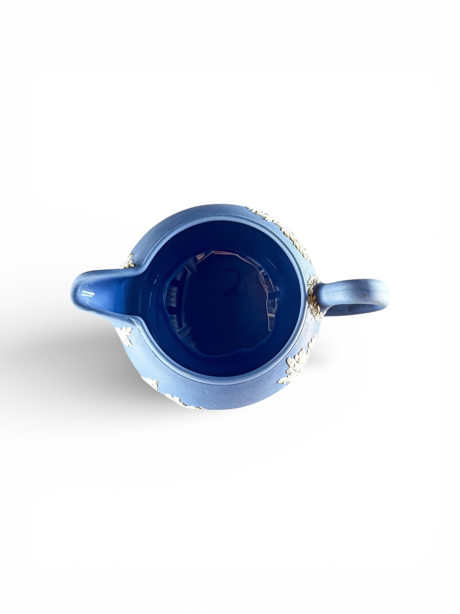 Top view of a blue ceramic pitcher with white floral relief details on a white background