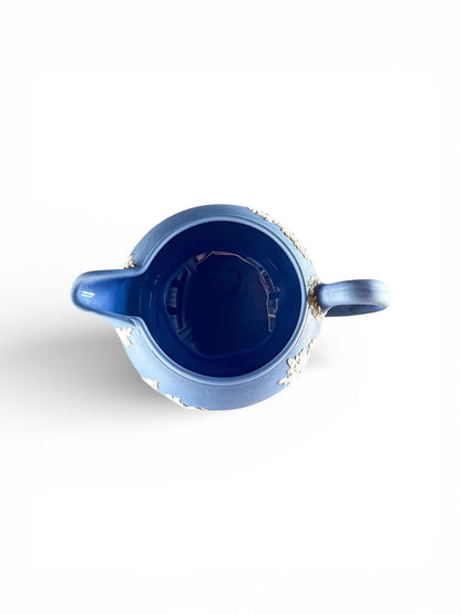 Top view of a blue ceramic pitcher with white floral relief details on a white background