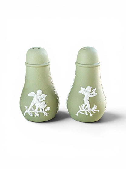 A pair of vintage Wedgwood sage green Jasperware salt and pepper shakers standing upright against a white background, displaying detailed white bas-relief classical cherubs on the front.