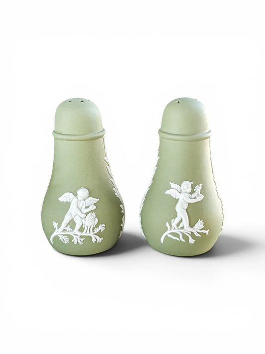 A pair of vintage Wedgwood sage green Jasperware salt and pepper shakers standing upright against a white background, displaying detailed white bas-relief classical cherubs on the front.