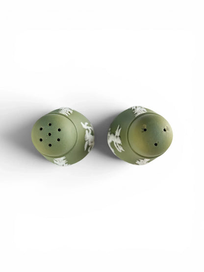 A top-down bird's-eye view of the vintage Wedgwood sage green Jasperware salt and pepper shakers, showcasing the distinct six-hole piercing pattern on the left shaker and the three-hole piercing pattern on the right shaker.