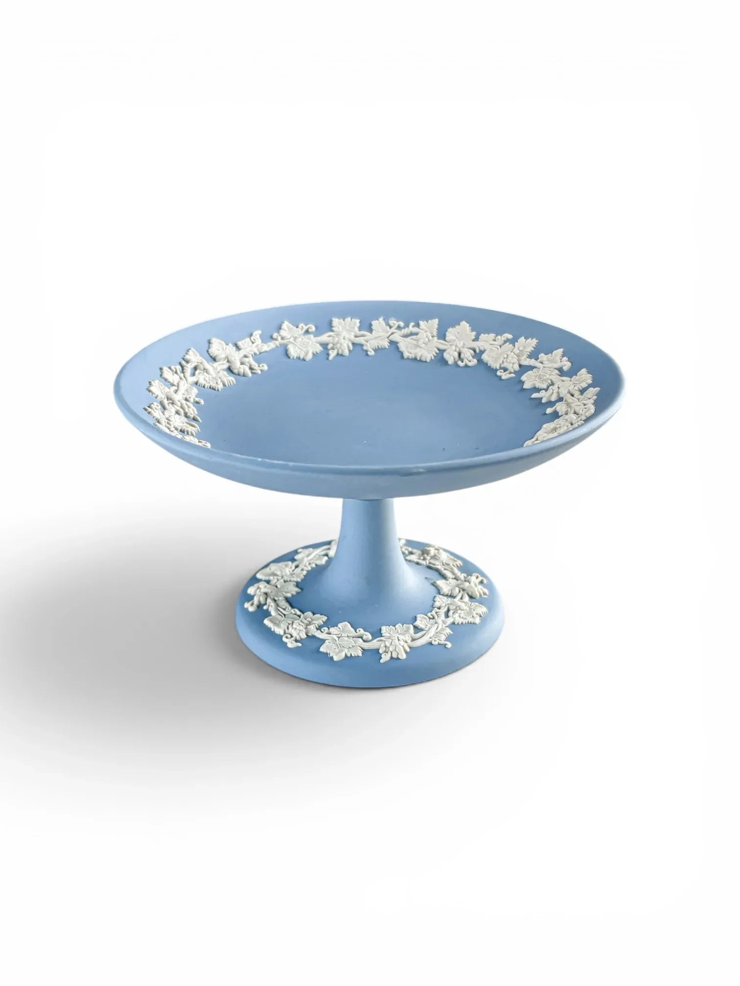 A high-angle view of a vintage pale blue Wedgwood Jasperware footed compote on a white background. This perspective showcases the wide, shallow bowl and the detailed "Vine and Leaf" white stoneware relief that accents the matte blue finish.