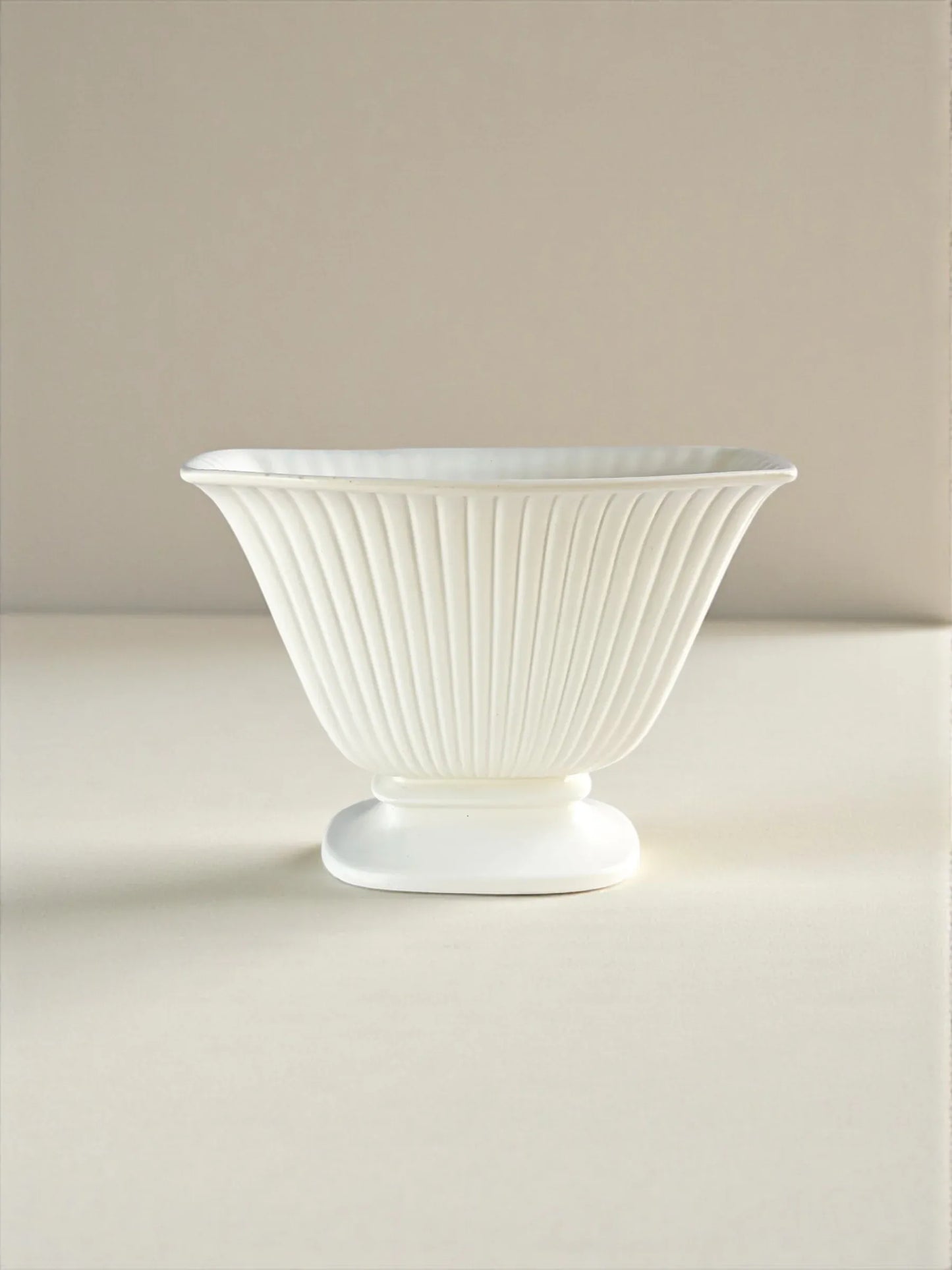 White fluted porcelain bowl with pedestal base on neutral background, elegant tableware.
