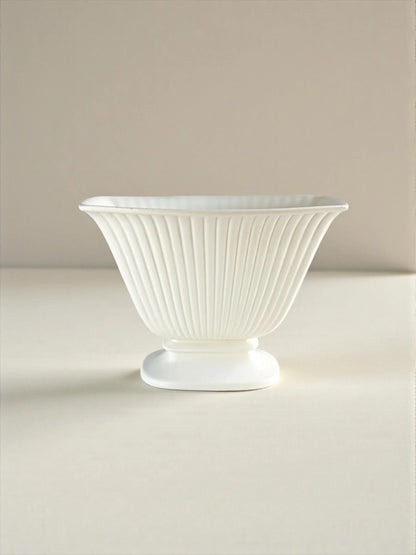 White fluted porcelain bowl with pedestal base on neutral background, elegant tableware.