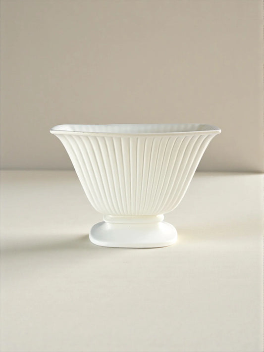 White fluted porcelain bowl with pedestal base on neutral background, elegant tableware.