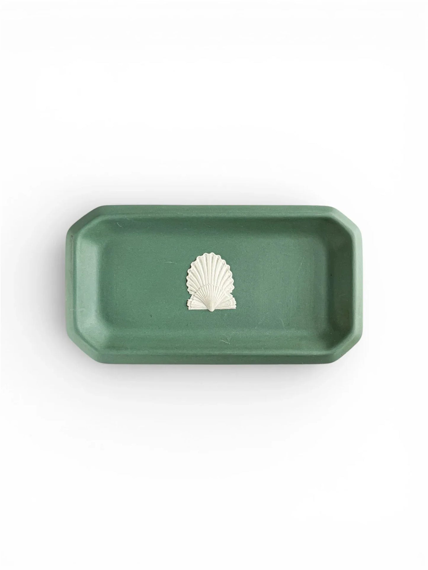 A top-down view of an oblong, octagonal Wedgwood Jasperware tray in deep Spruce Green, featuring a single white bas-relief scallop shell motif in the centre against a plain white background.