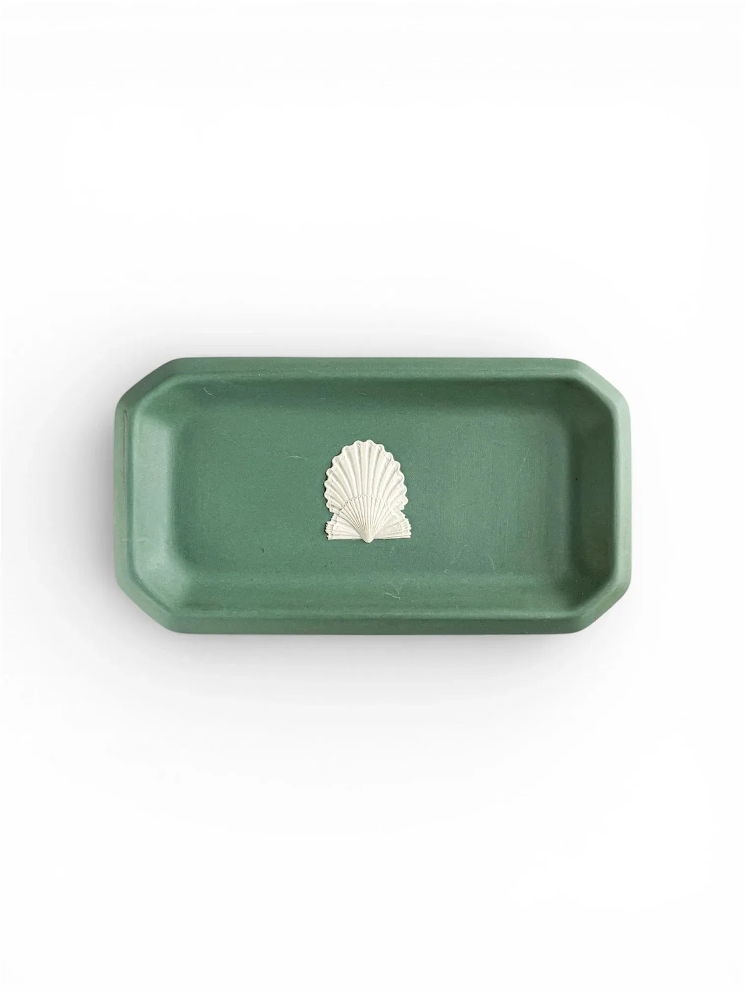 A top-down view of an oblong, octagonal Wedgwood Jasperware tray in deep Spruce Green, featuring a single white bas-relief scallop shell motif in the centre against a plain white background.