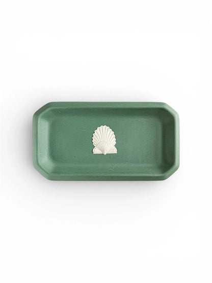 A top-down view of an oblong, octagonal Wedgwood Jasperware tray in deep Spruce Green, featuring a single white bas-relief scallop shell motif in the centre against a plain white background.