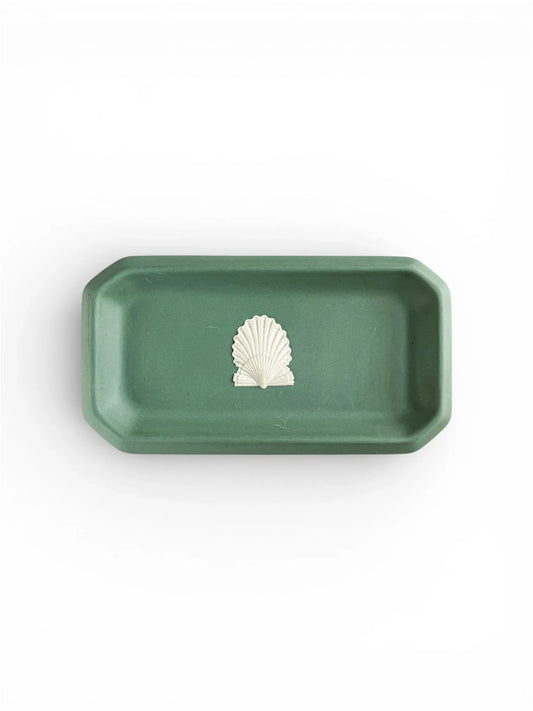 A top-down view of an oblong, octagonal Wedgwood Jasperware tray in deep Spruce Green, featuring a single white bas-relief scallop shell motif in the centre against a plain white background.