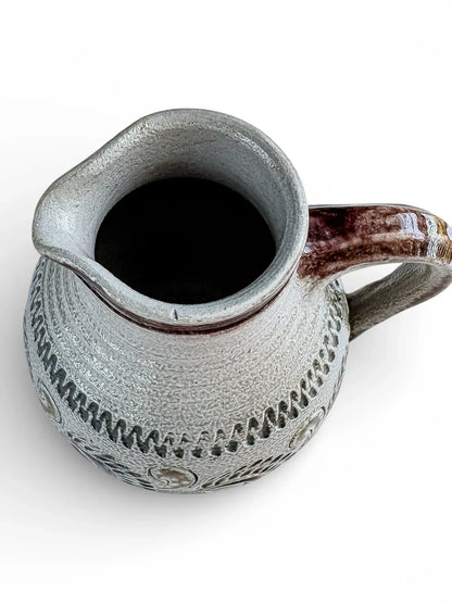 Vintage ceramic pitcher with textured gray pattern and brown handle on white background