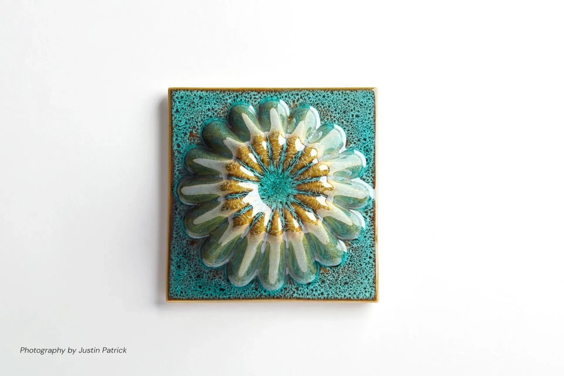 A top-down close-up of a single square ceramic tile. The piece features a circular, fluted dome in the centre with a reactive green glaze.