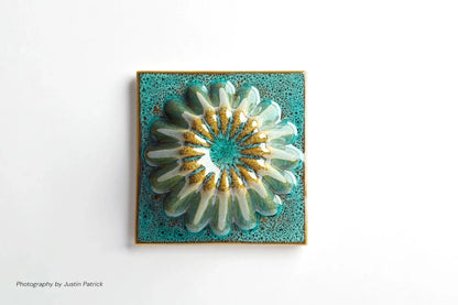 A top-down close-up of a single square ceramic tile. The piece features a circular, fluted dome in the centre with a reactive green glaze.