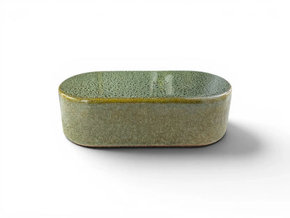 A front-angled view of a single Wiid Design rounded ceramic brick on a white background. The high-gloss reactive green glaze shows a dense, variegated "frosted" pattern, highlighting the smooth, pill-shaped silhouette of the earthenware piece.