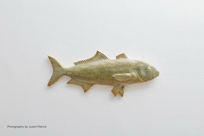 A side-profile view of the sculptural Ice Fish in forest green reactive glaze. The ceramic fish features a more muted, mossy green finish with subtle amber highlights on the edges of the fins and tail.