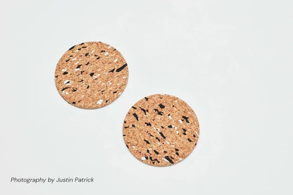 Top-down view of two Wiid Design cork coasters in the black-and-white speckled variant. The light composite cork is patterned with recycled black and white rubber granules, showing a clean, circular silhouette.