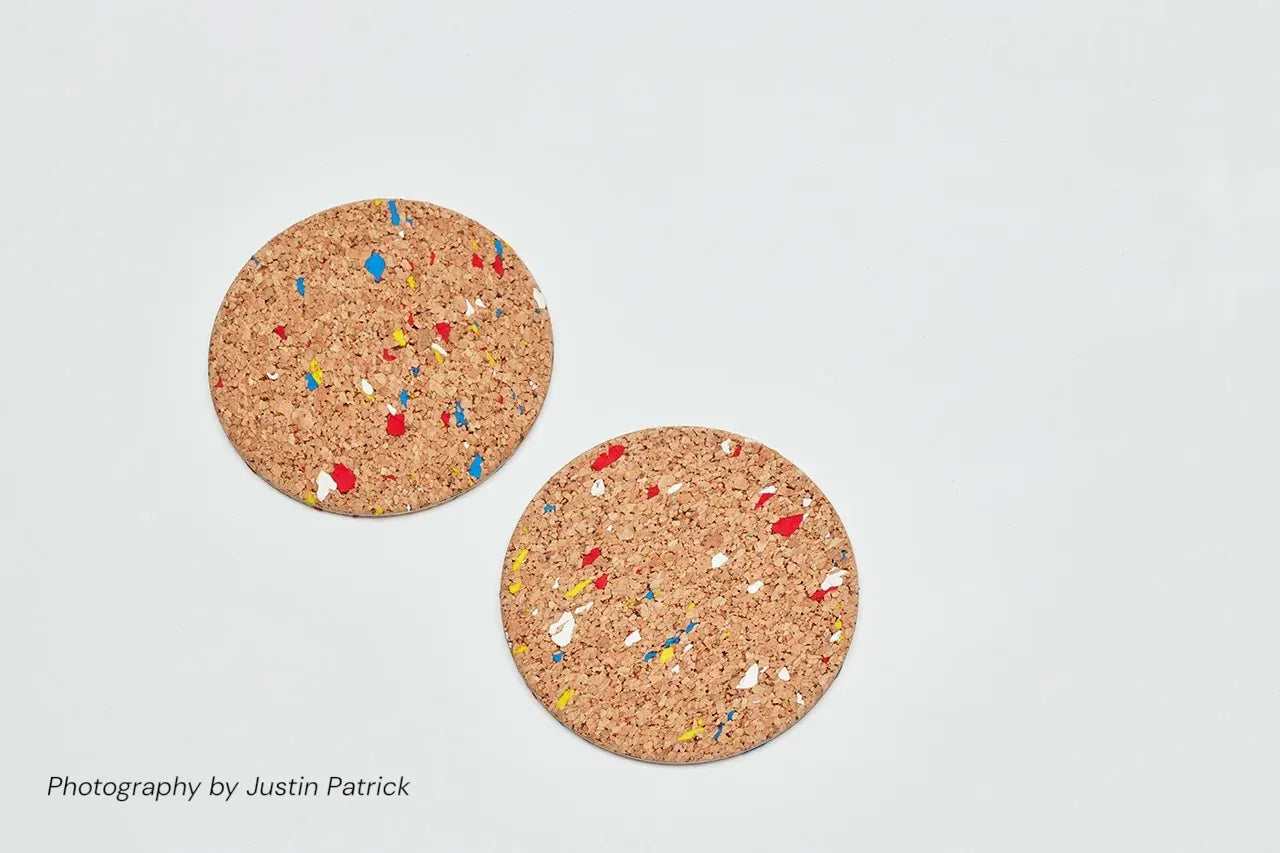 Top-down view of two Wiid Design cork coasters in the multi-colour speckled variant. The natural light cork is scattered with recycled rubber flecks in vibrant blue, red, and yellow, creating a terrazzo-style finish.